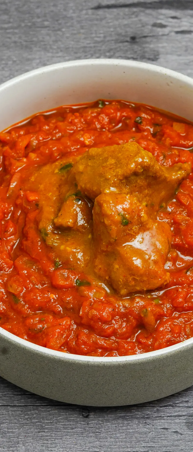 Chicken curry featuring pieces of chicken in a vibrant red tomato-based sauce, served in a white bowl.