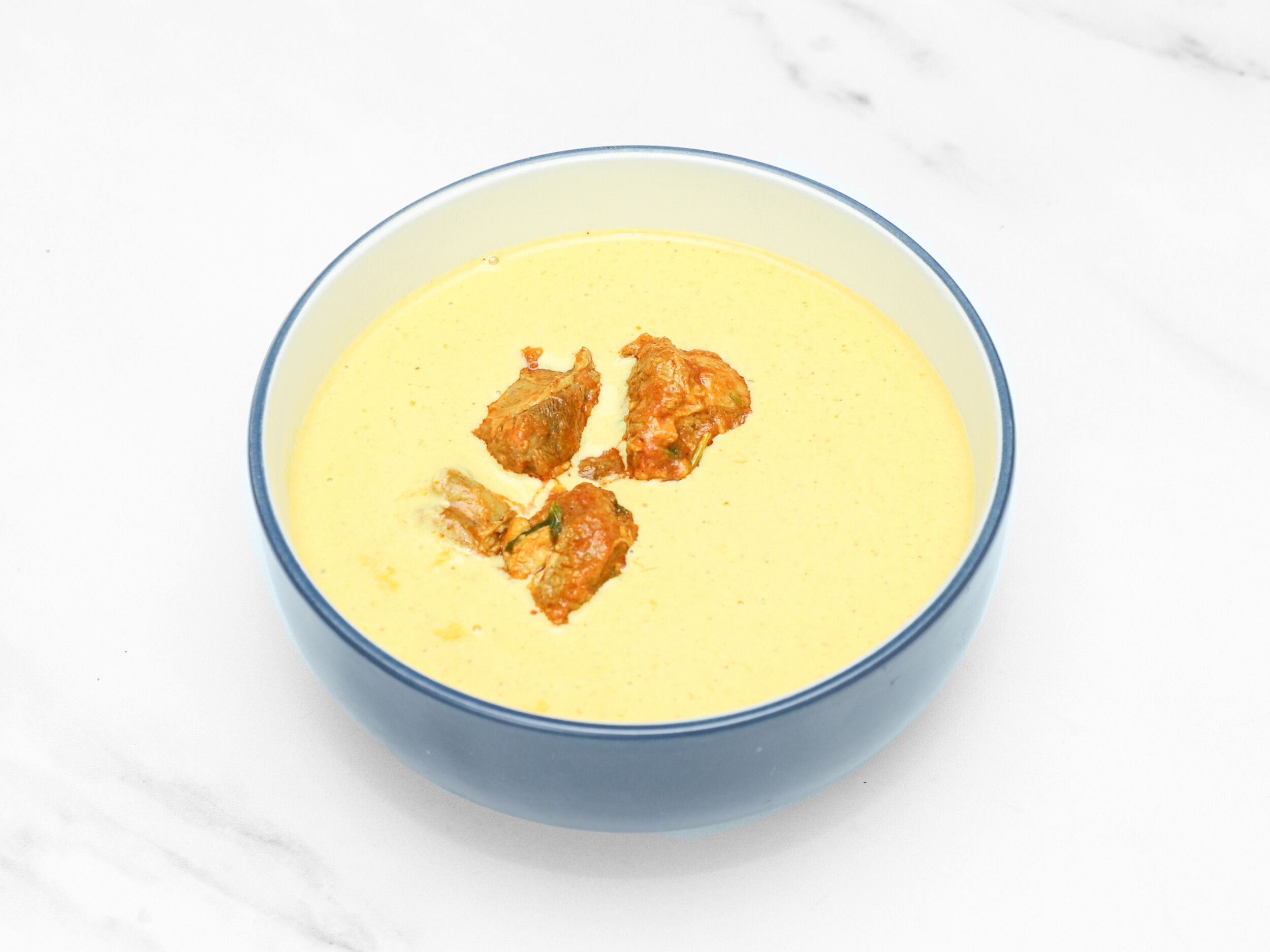 Four golden brown pakora pieces floating in a vibrant yellow kadhi sauce in a blue bowl.
