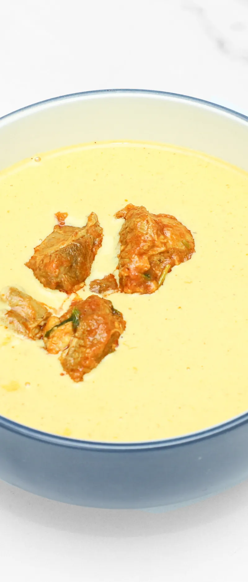 Four golden brown pakora pieces floating in a vibrant yellow kadhi sauce in a blue bowl.