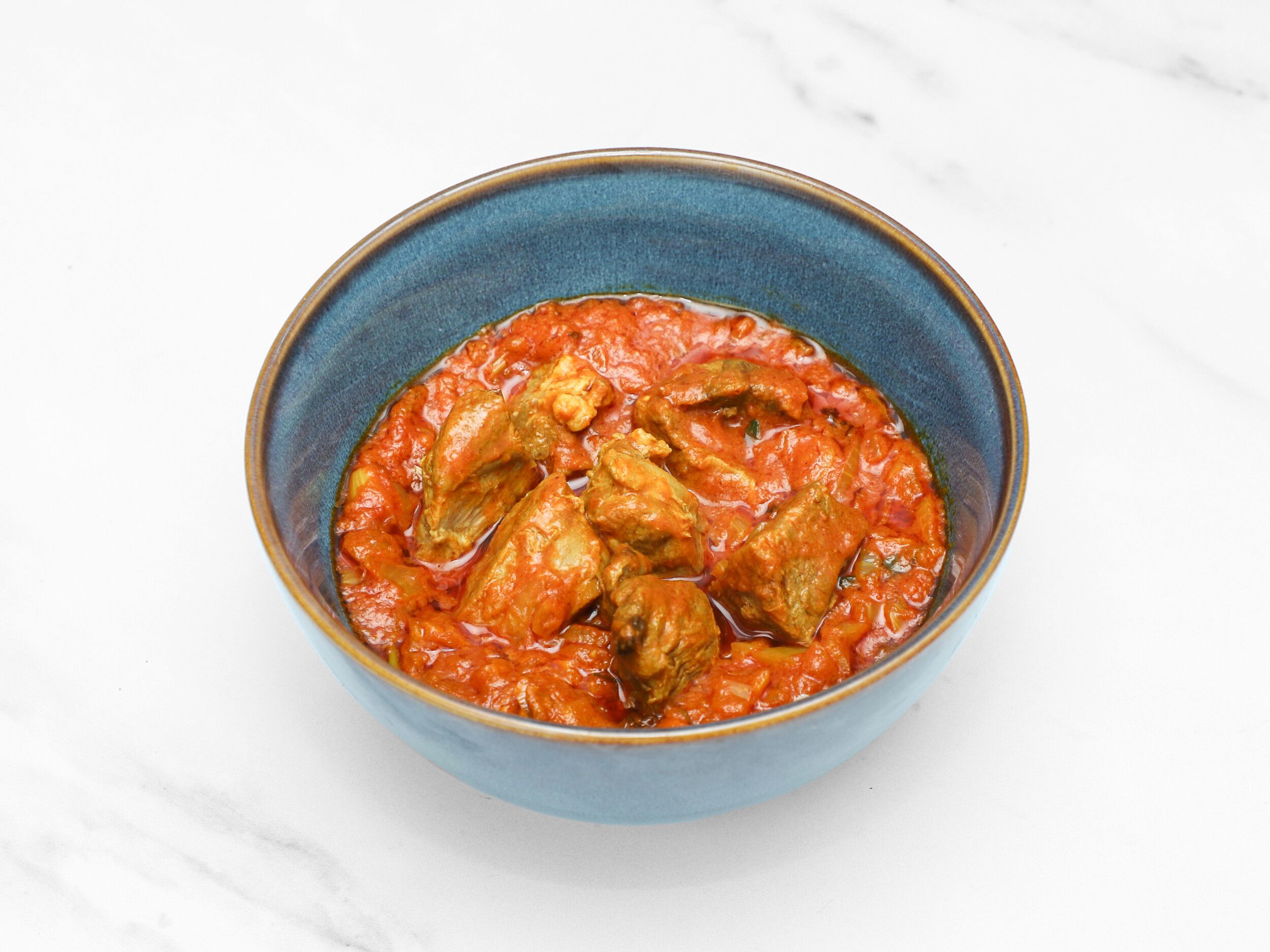 Lamb bhuna with chunks of meat in a thick, red-orange tomato-based sauce, served in a blue bowl.