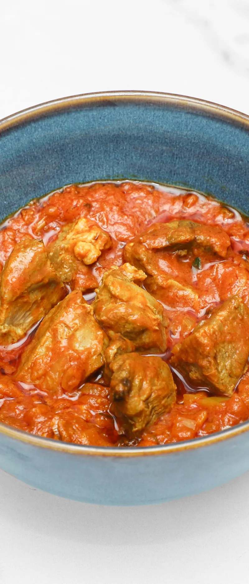 Lamb bhuna with chunks of meat in a thick, red-orange tomato-based sauce, served in a blue bowl.