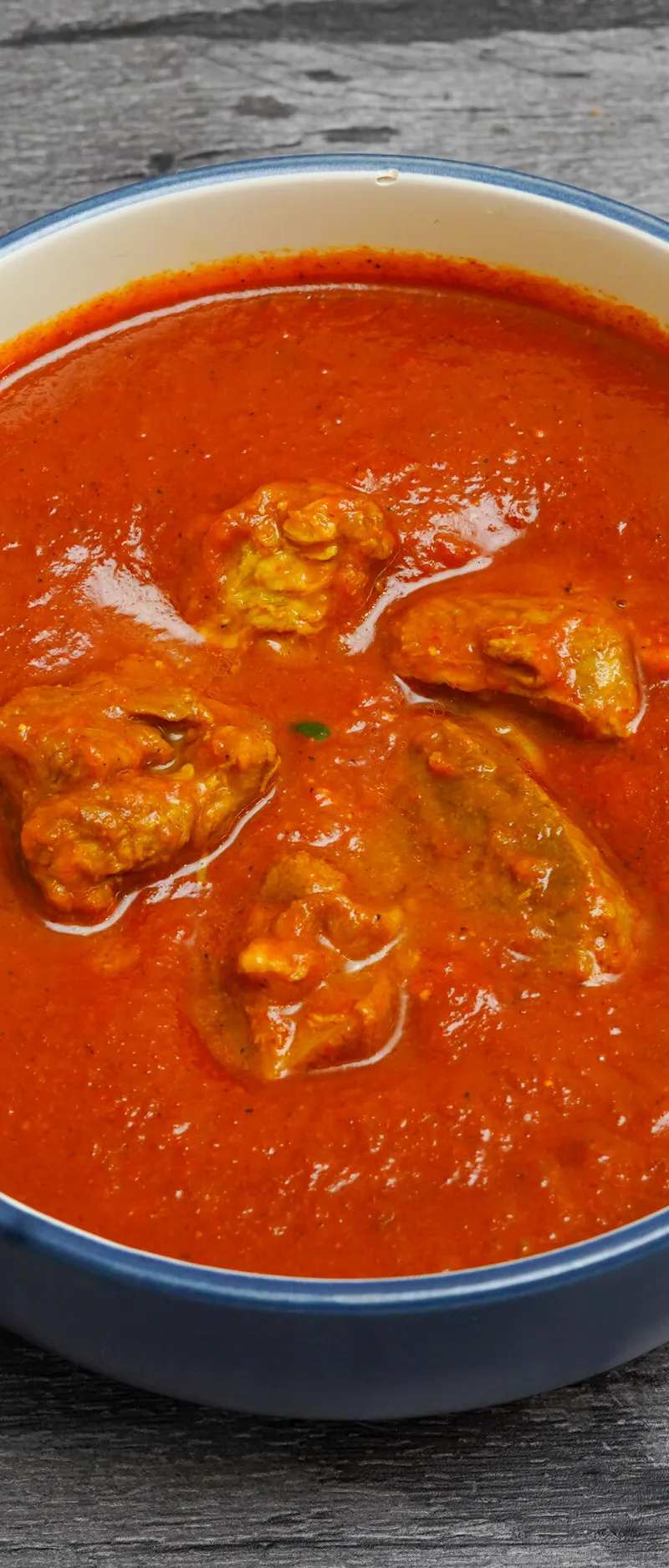 Chicken curry with chunks of meat in a vibrant red sauce, served in a blue and white ceramic bowl.