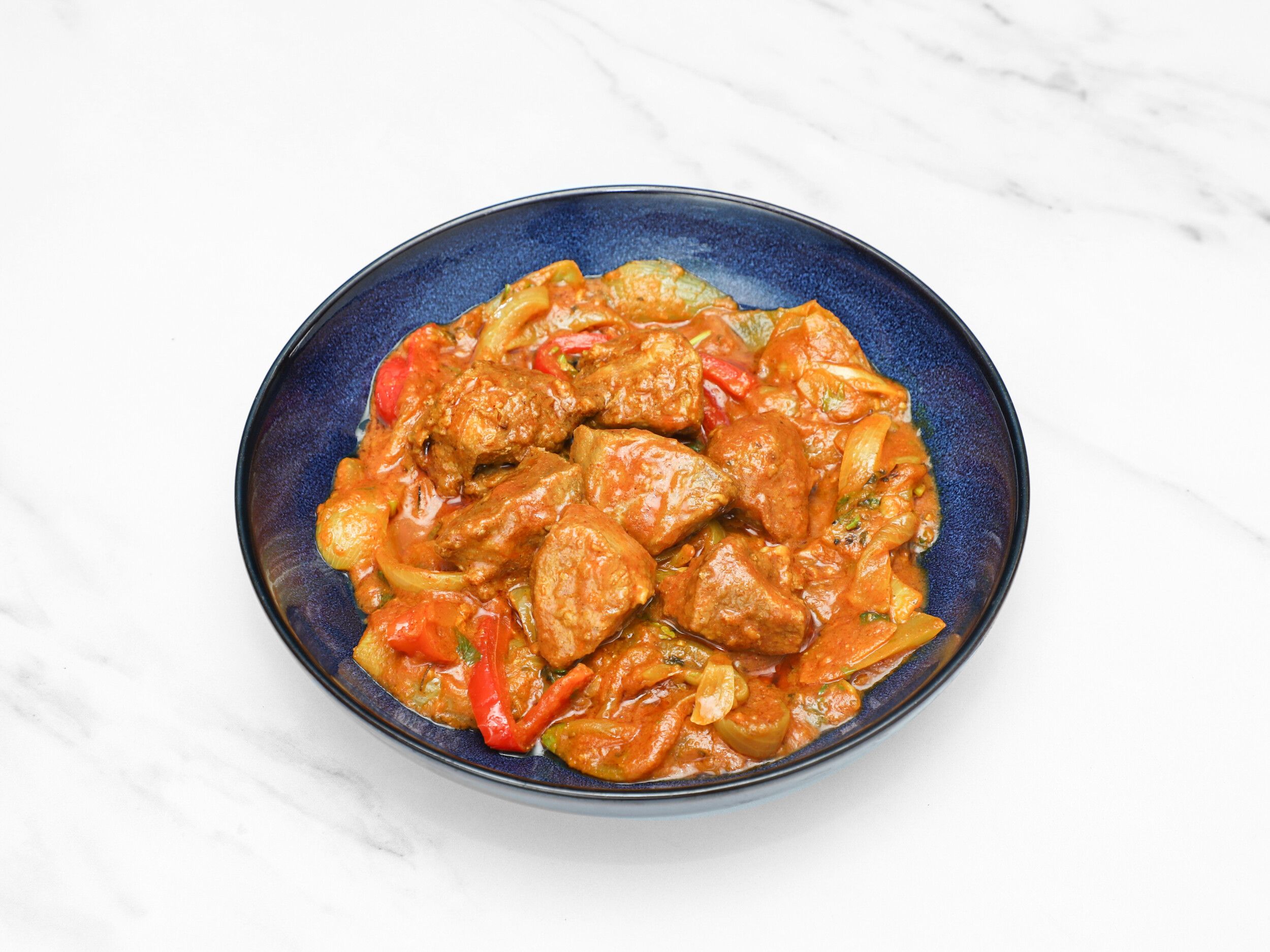 Beef karahi with red bell peppers and onions in a rich orange gravy, served in a deep blue bowl.