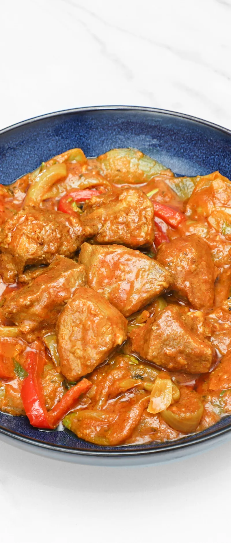 Beef karahi with red bell peppers and onions in a rich orange gravy, served in a deep blue bowl.