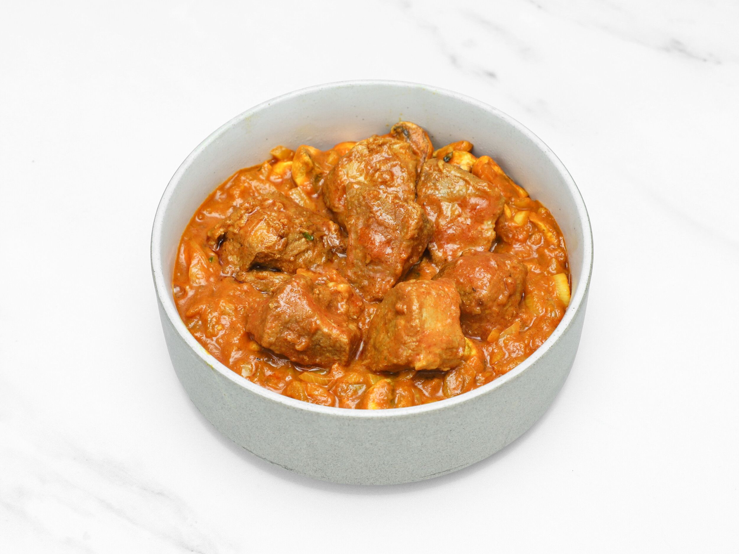 Lamb curry with tender meat pieces and a rich orange sauce, served in a grey bowl.