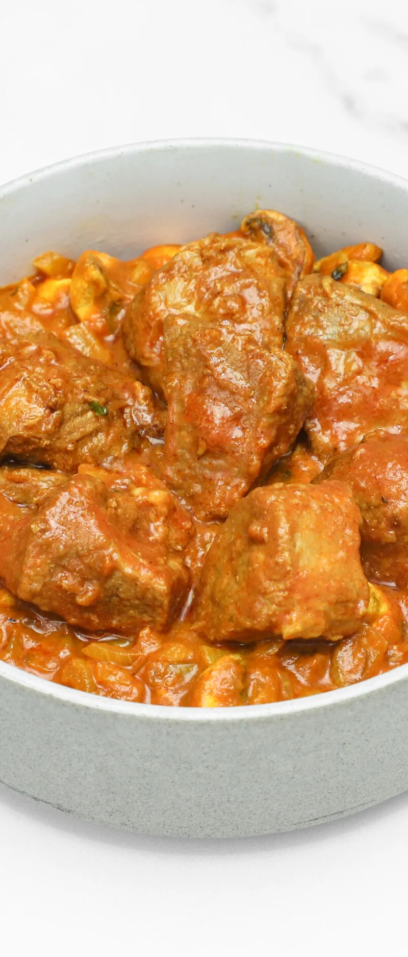 Lamb curry with tender meat pieces and a rich orange sauce, served in a grey bowl.