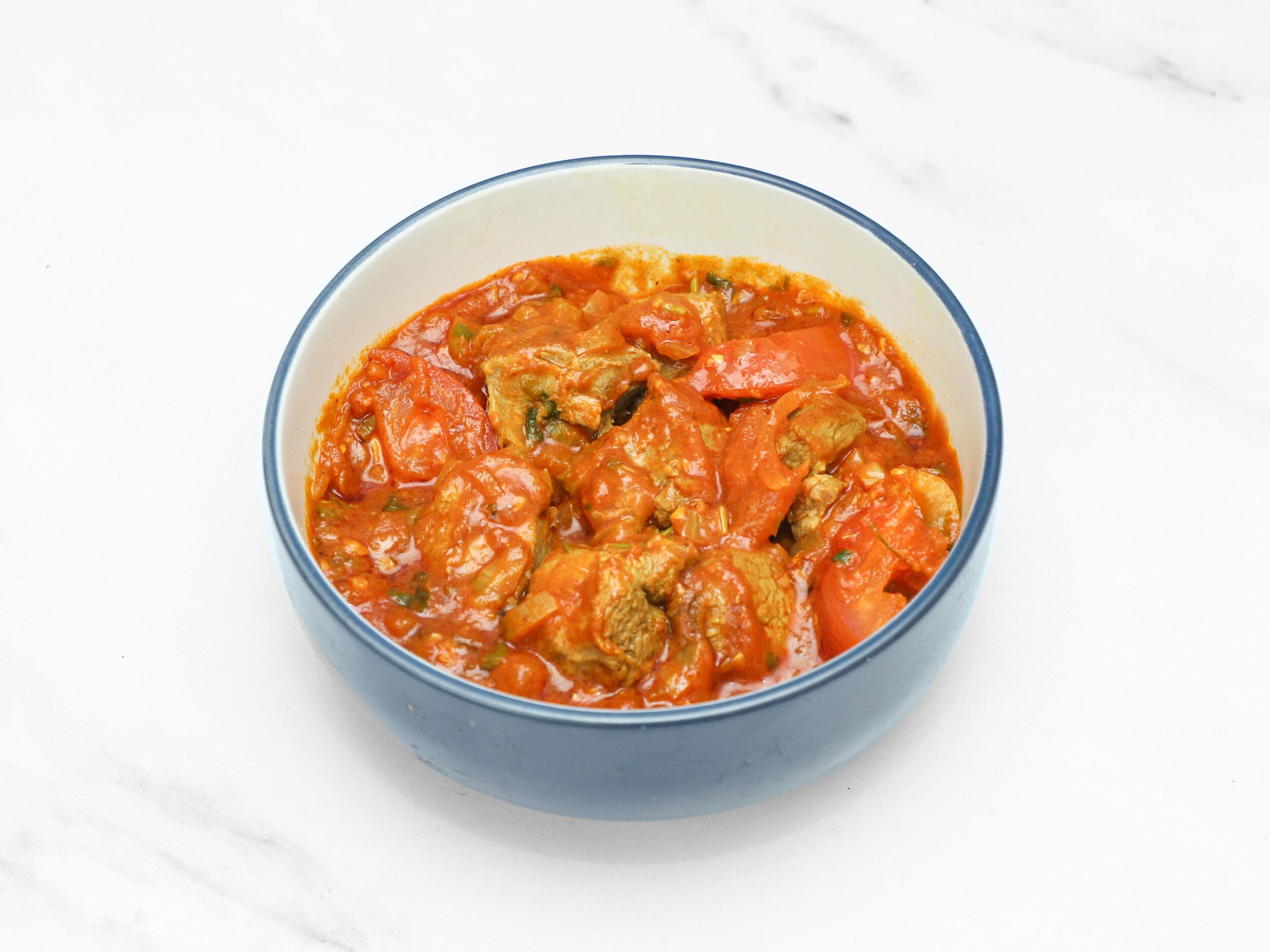 Lamb bhuna in a blue and white ceramic bowl with visible chunks of tomatoes and meat