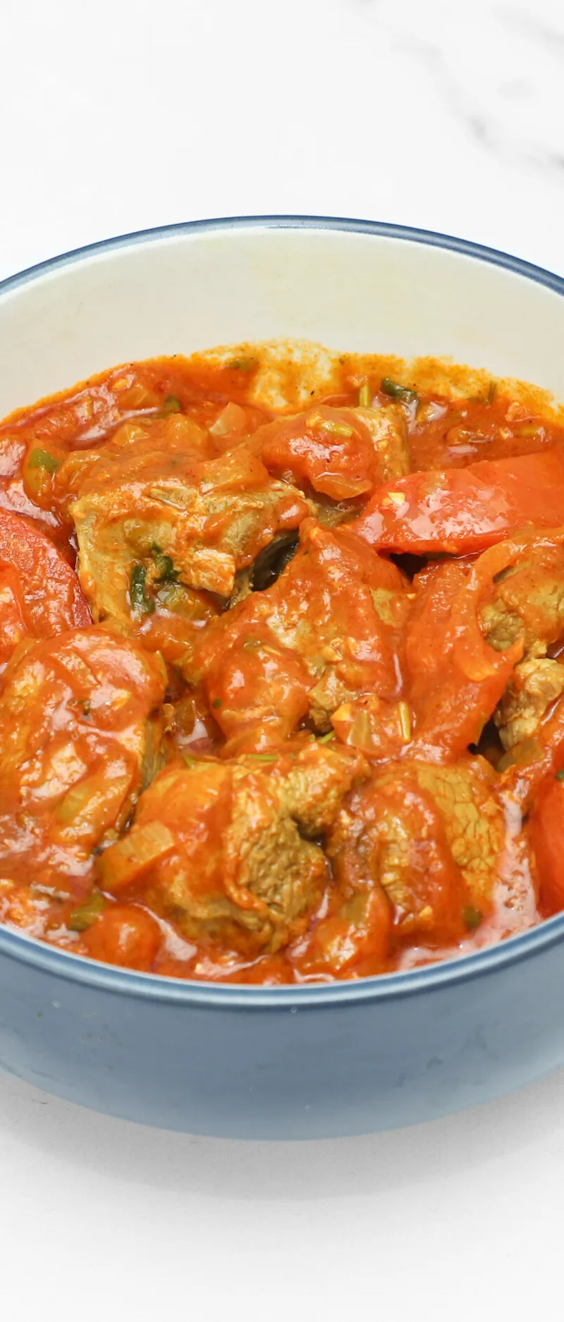 Lamb bhuna in a blue and white ceramic bowl with visible chunks of tomatoes and meat