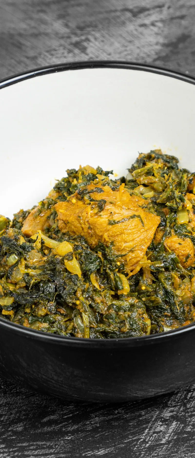 Sag chicken curry in a black and white bowl, on a dark textured surface