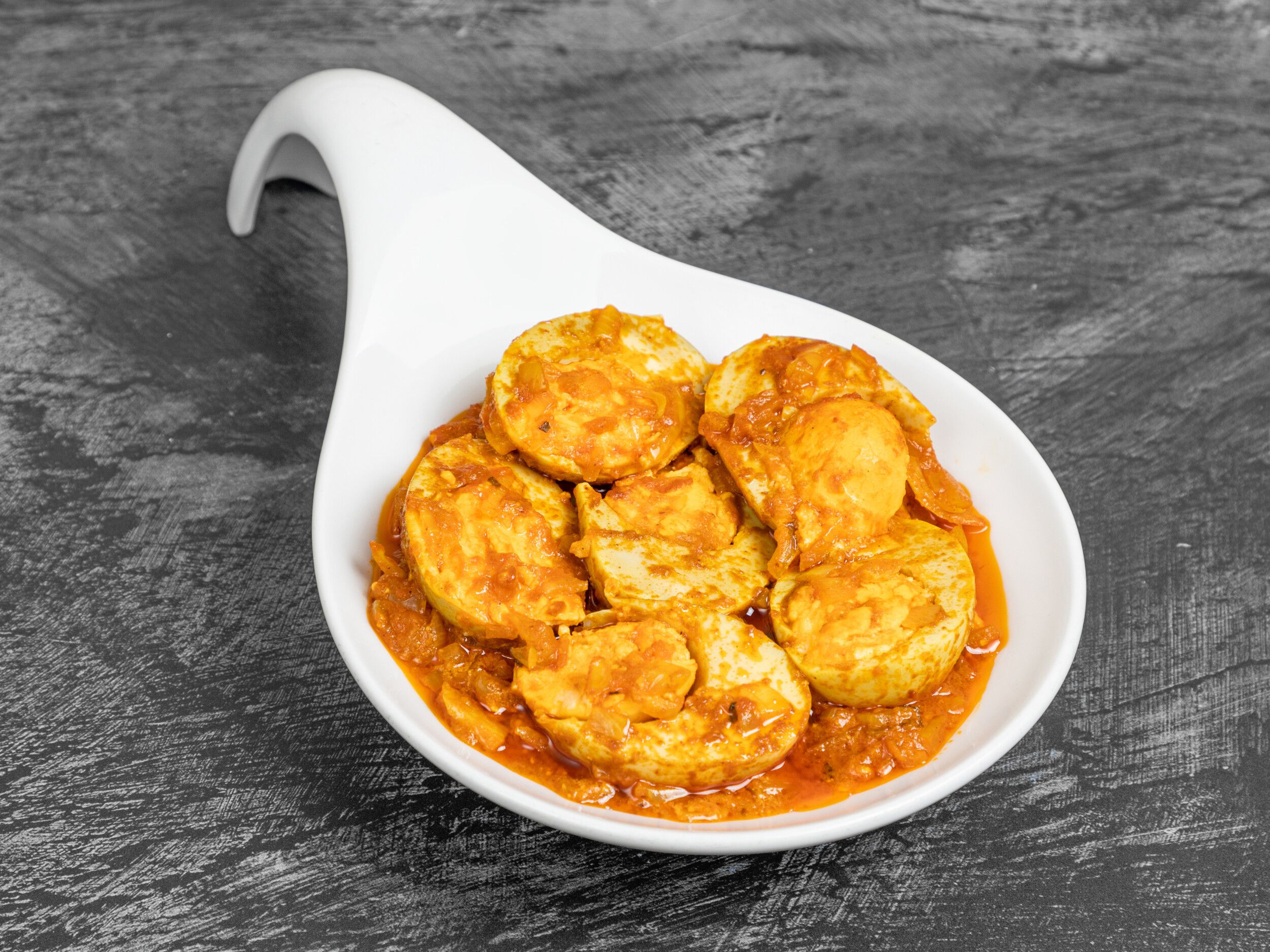 Halved boiled eggs in a thick orange curry sauce with onions, served in a white dish.