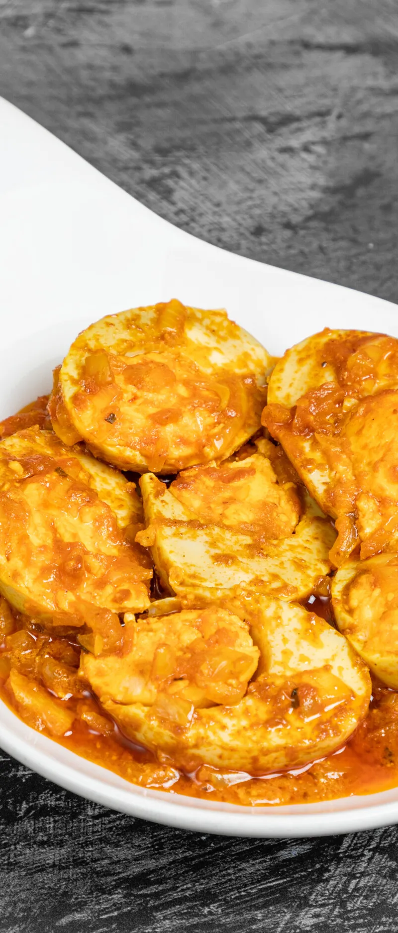 Halved boiled eggs in a thick orange curry sauce with onions, served in a white dish.