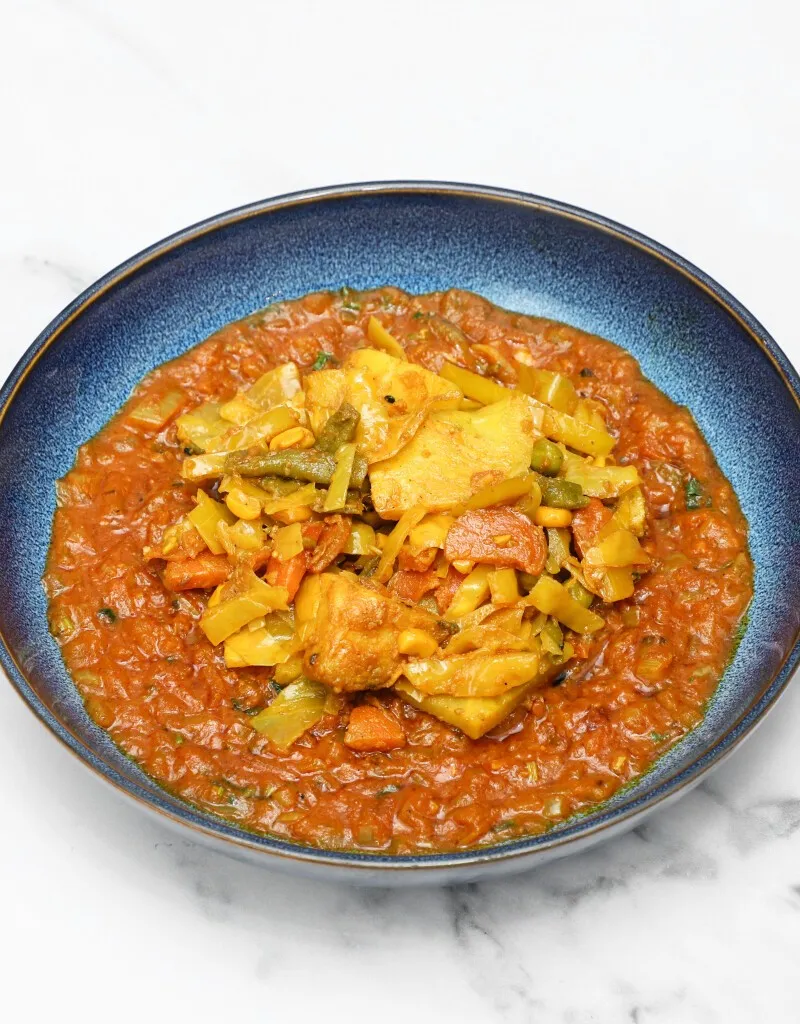 Top-down view of a colorful vegetable and chicken curry in a deep blue bowl on a white surface.