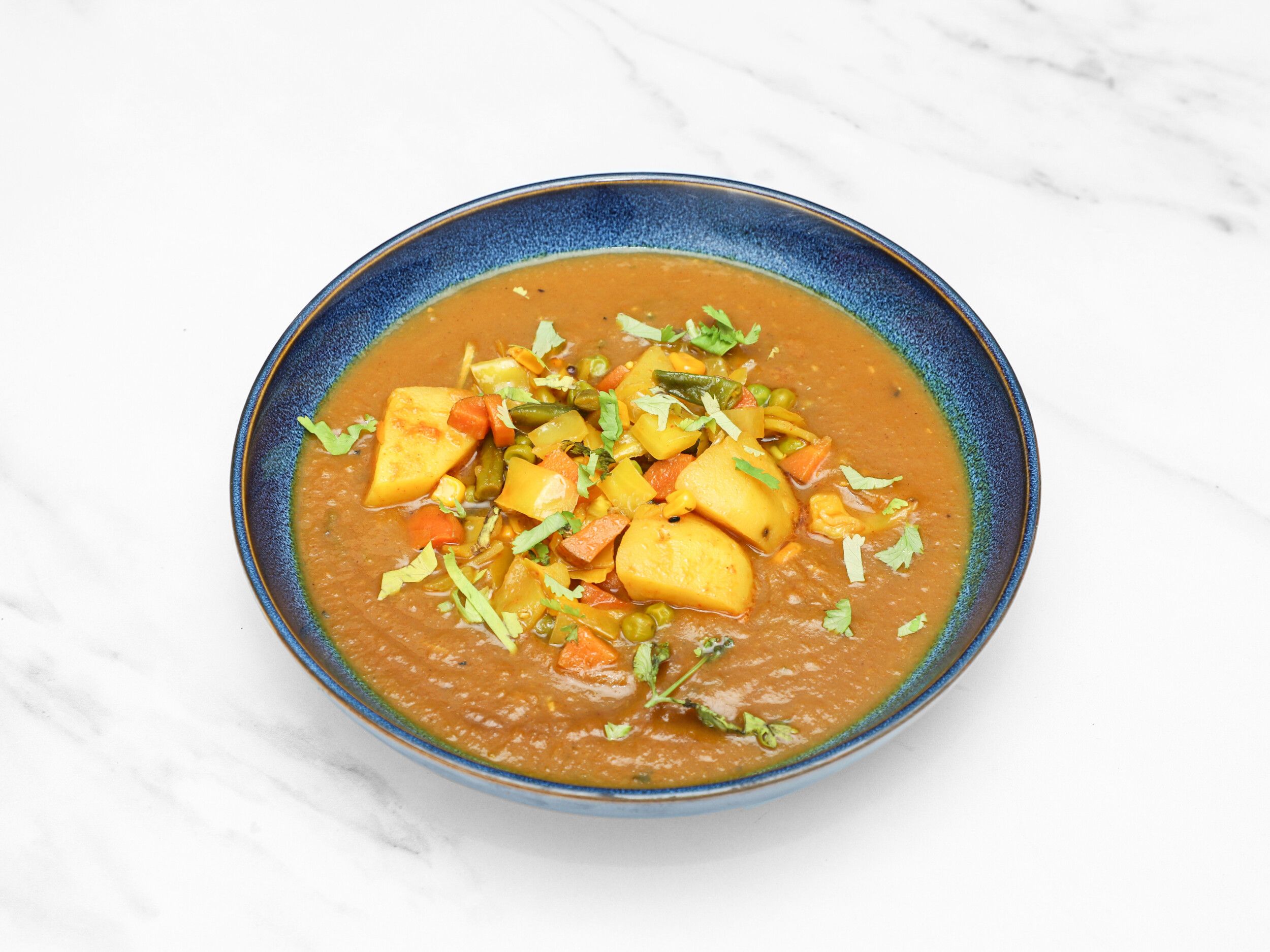 Indian vegetable curry with potatoes, peas, carrots, and green beans in a rustic blue bowl.