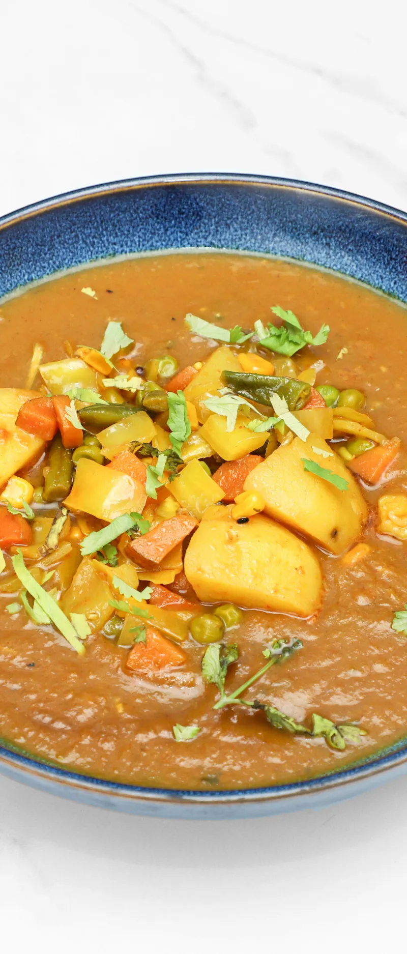 Indian vegetable curry with potatoes, peas, carrots, and green beans in a rustic blue bowl.