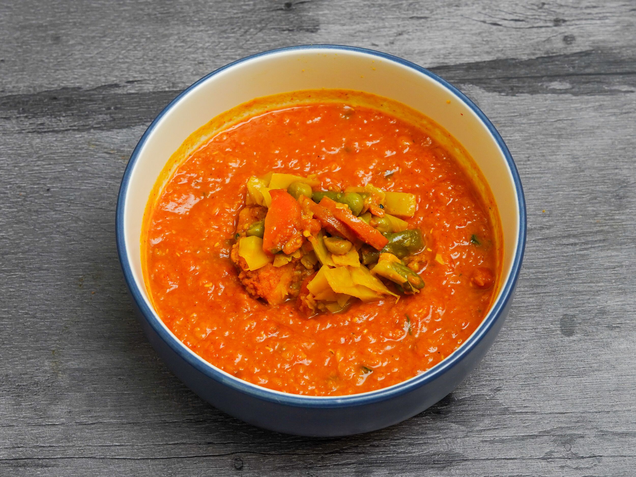 Bright orange curry with mixed vegetables including carrots, peas, and yellow pieces in a blue-rimmed bowl