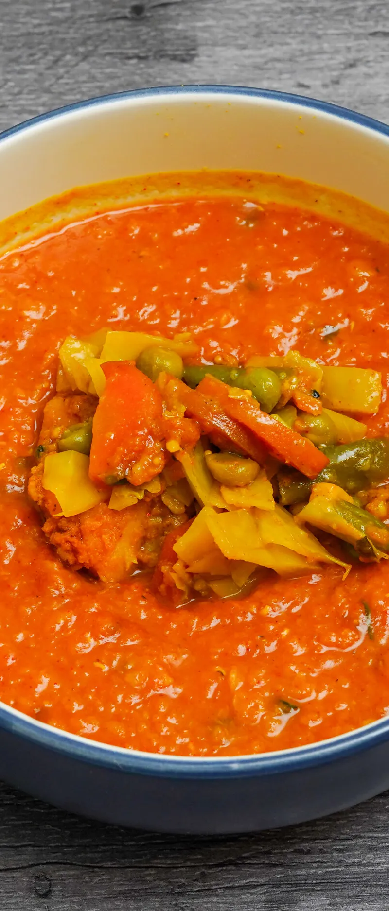Bright orange curry with mixed vegetables including carrots, peas, and yellow pieces in a blue-rimmed bowl