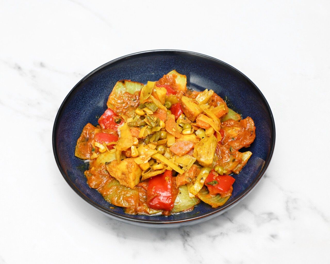 Mixed vegetable bhaji in a dark blue bowl, featuring potatoes, bell peppers, carrots, and peas.