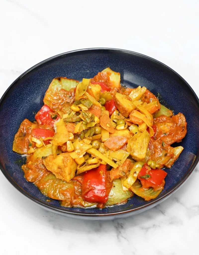 Mixed vegetable bhaji in a dark blue bowl, featuring potatoes, bell peppers, carrots, and peas.