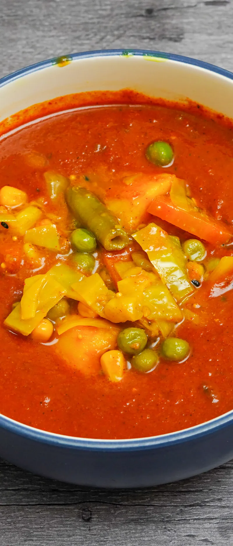 A close-up of a colorful vegetable curry in a blue bowl on a textured grey surface.