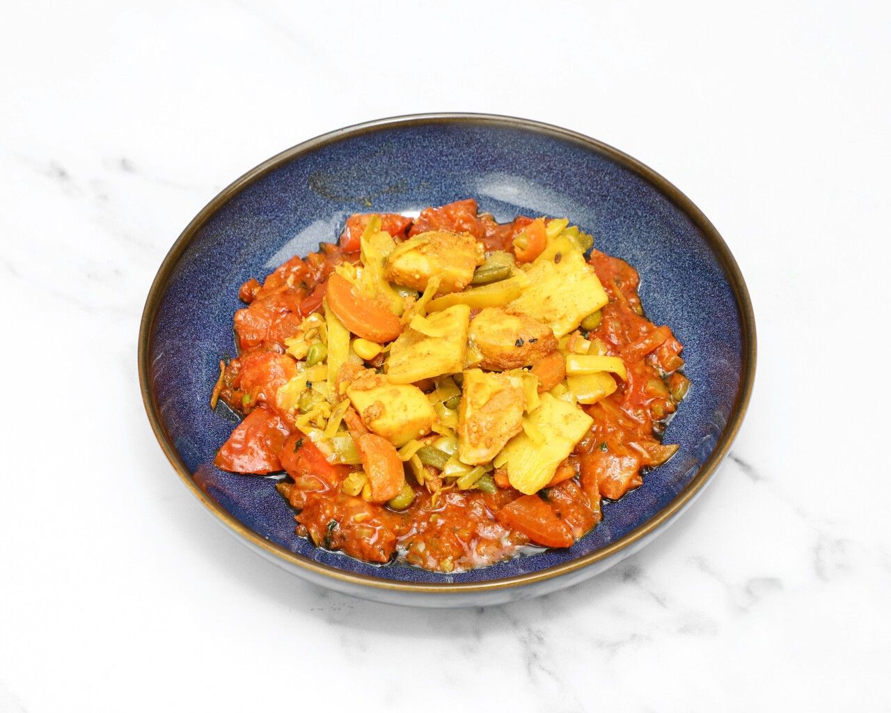 Indian vegetable curry in a blue bowl with paneer, carrots, cabbage, and red sauce.