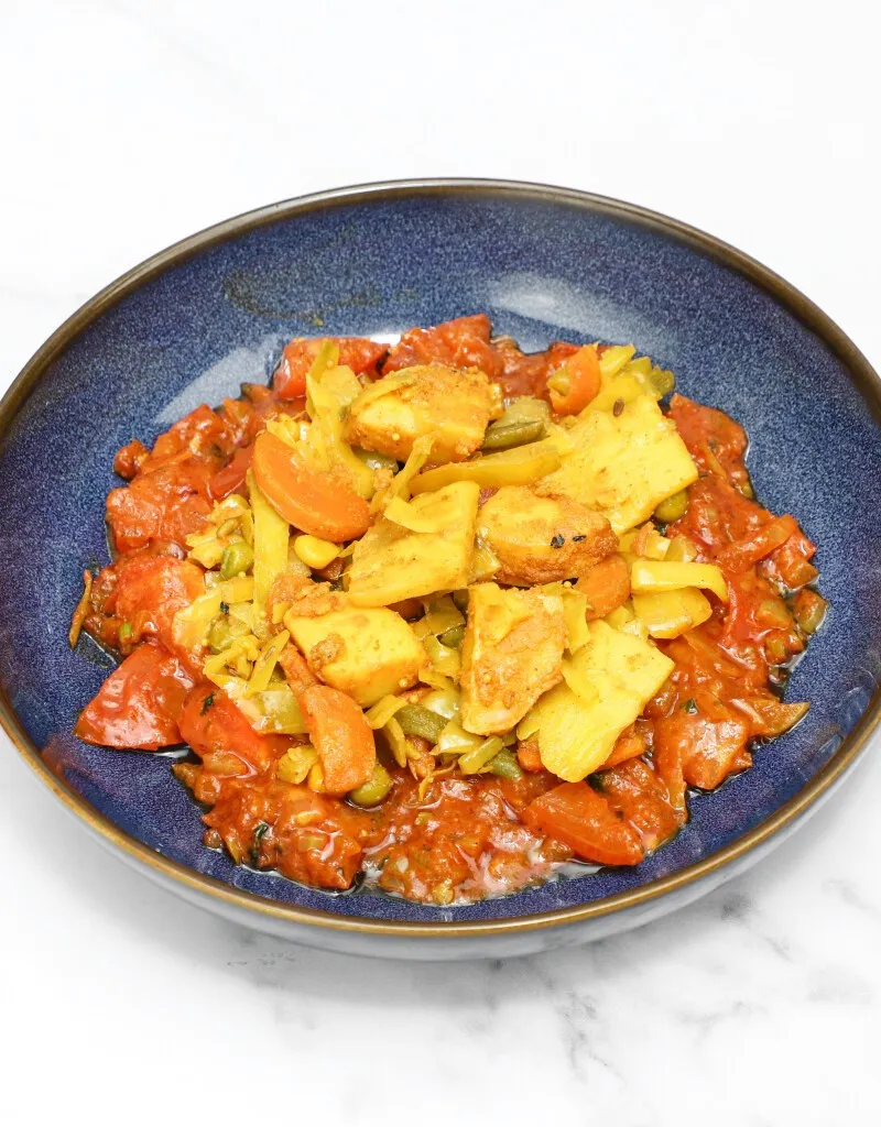 Indian vegetable curry in a blue bowl with paneer, carrots, cabbage, and red sauce.