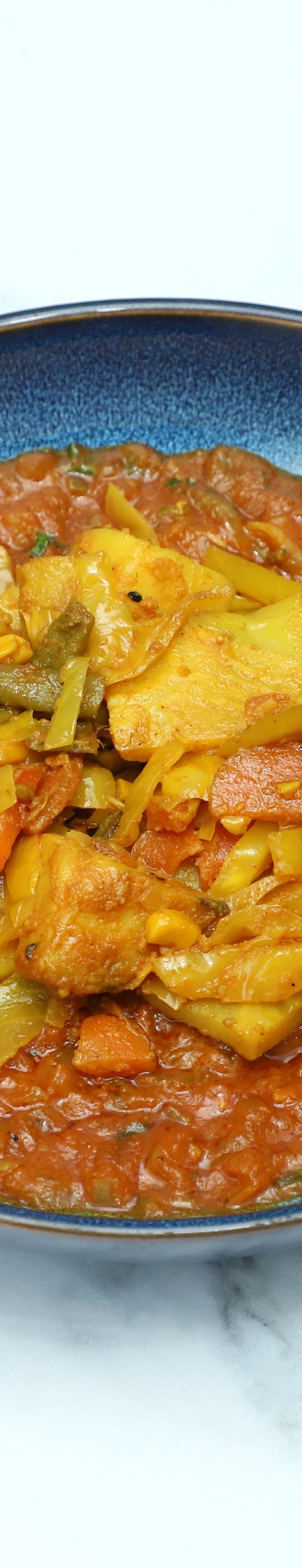 A close-up view of a vibrant vegetable curry in a blue ceramic bowl on a white marble surface.