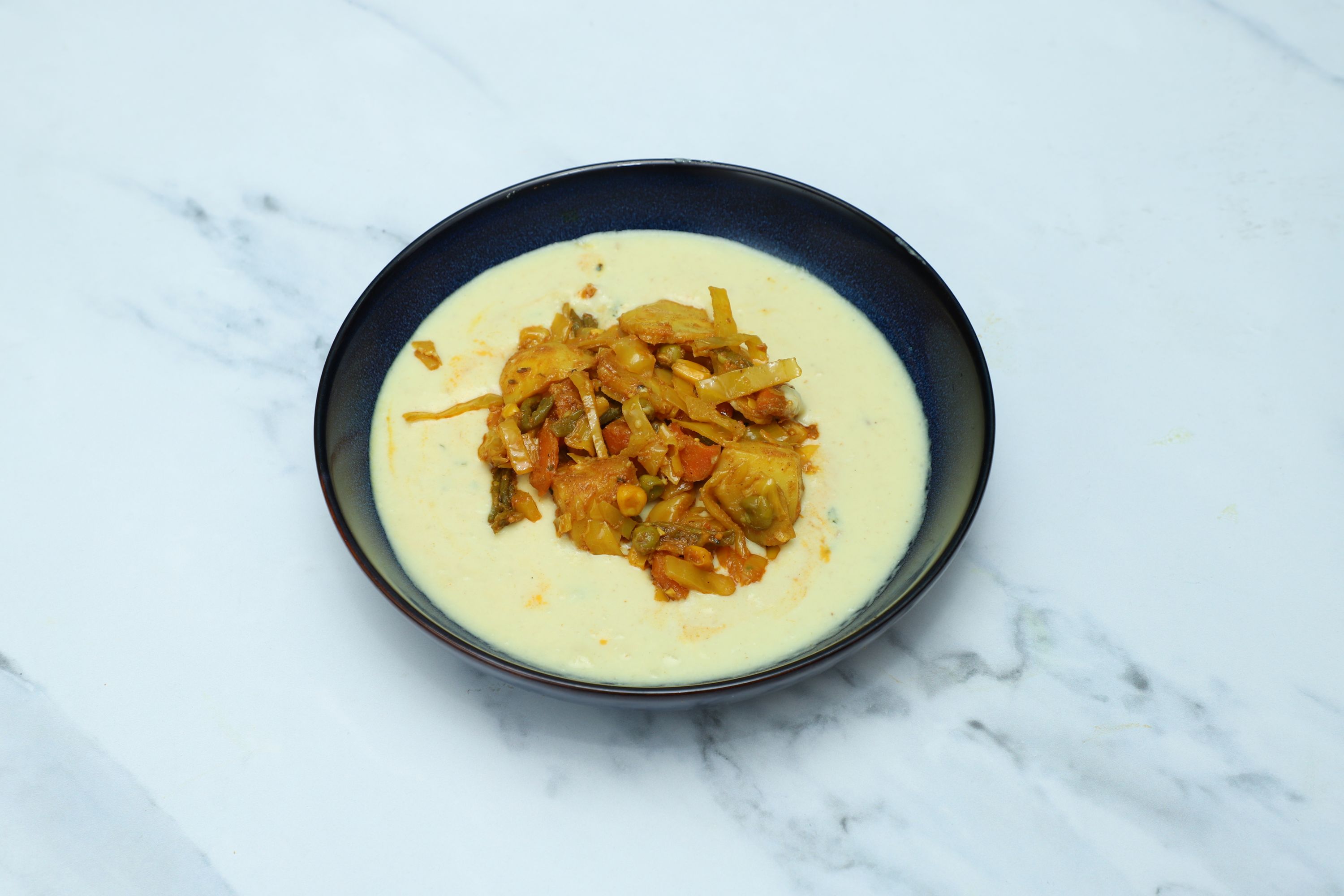 A black bowl of creamy yellow curry with a central topping of mixed vegetable curry.