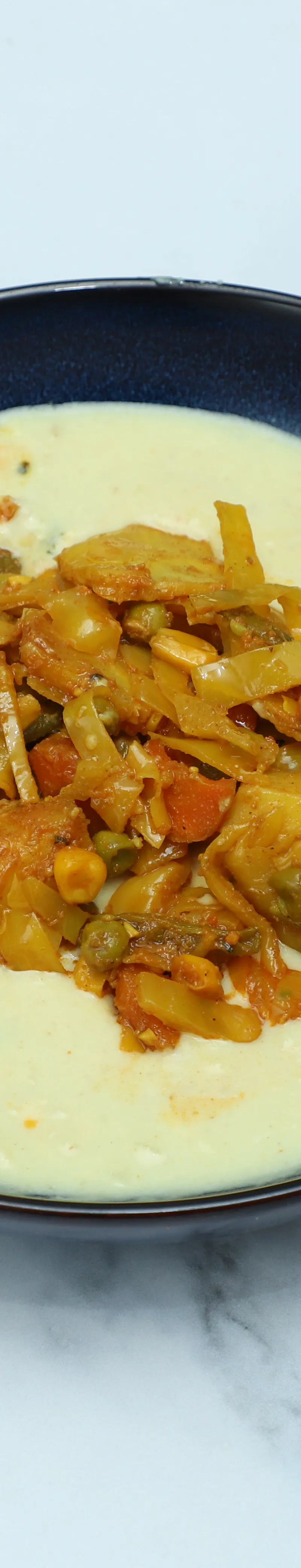 A black bowl of creamy yellow curry with a central topping of mixed vegetable curry.
