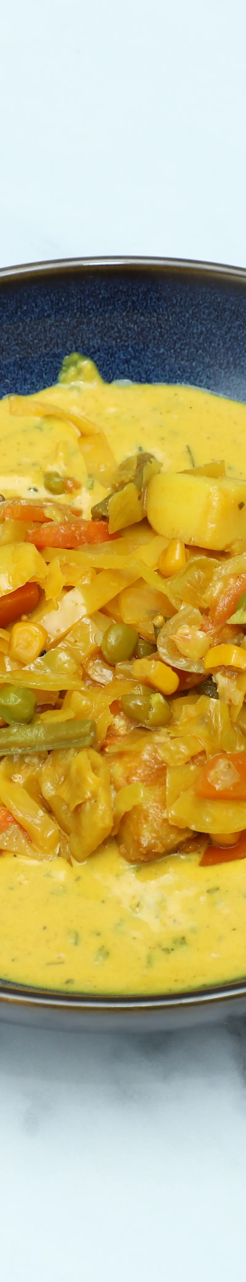 A dark blue bowl filled with a creamy yellow vegetable curry, showcasing visible carrots, peas, and potatoes.