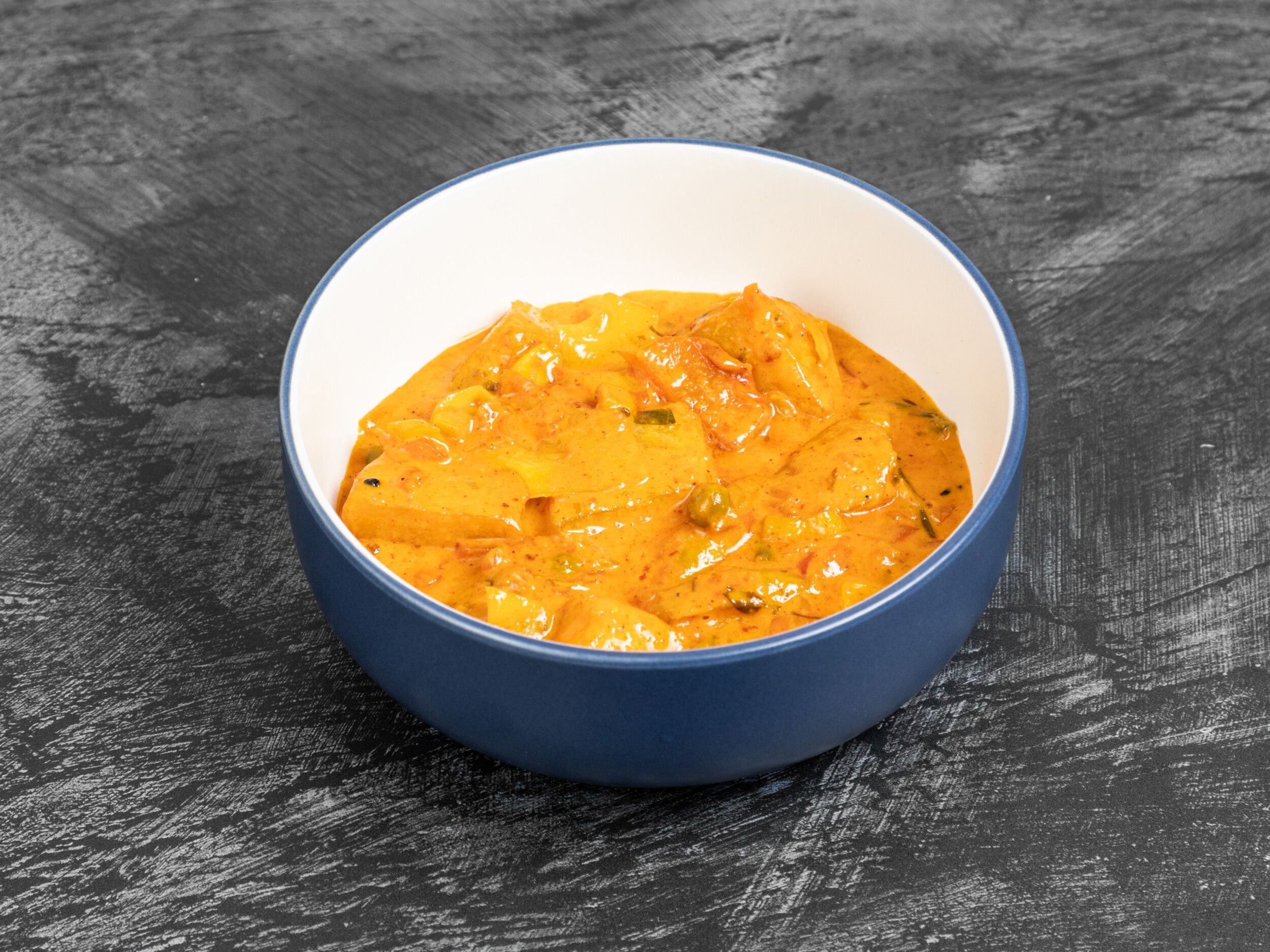 A deep blue and white bowl filled with an orangey-yellow Kashmiri aloo gobi curry