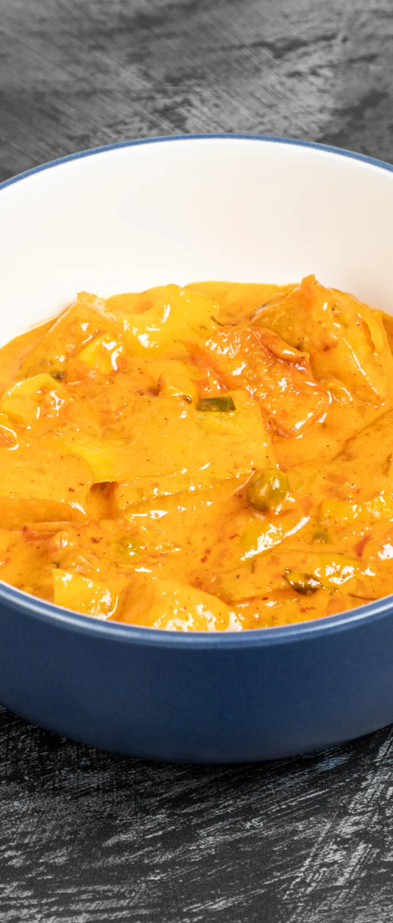 A deep blue and white bowl filled with an orangey-yellow Kashmiri aloo gobi curry