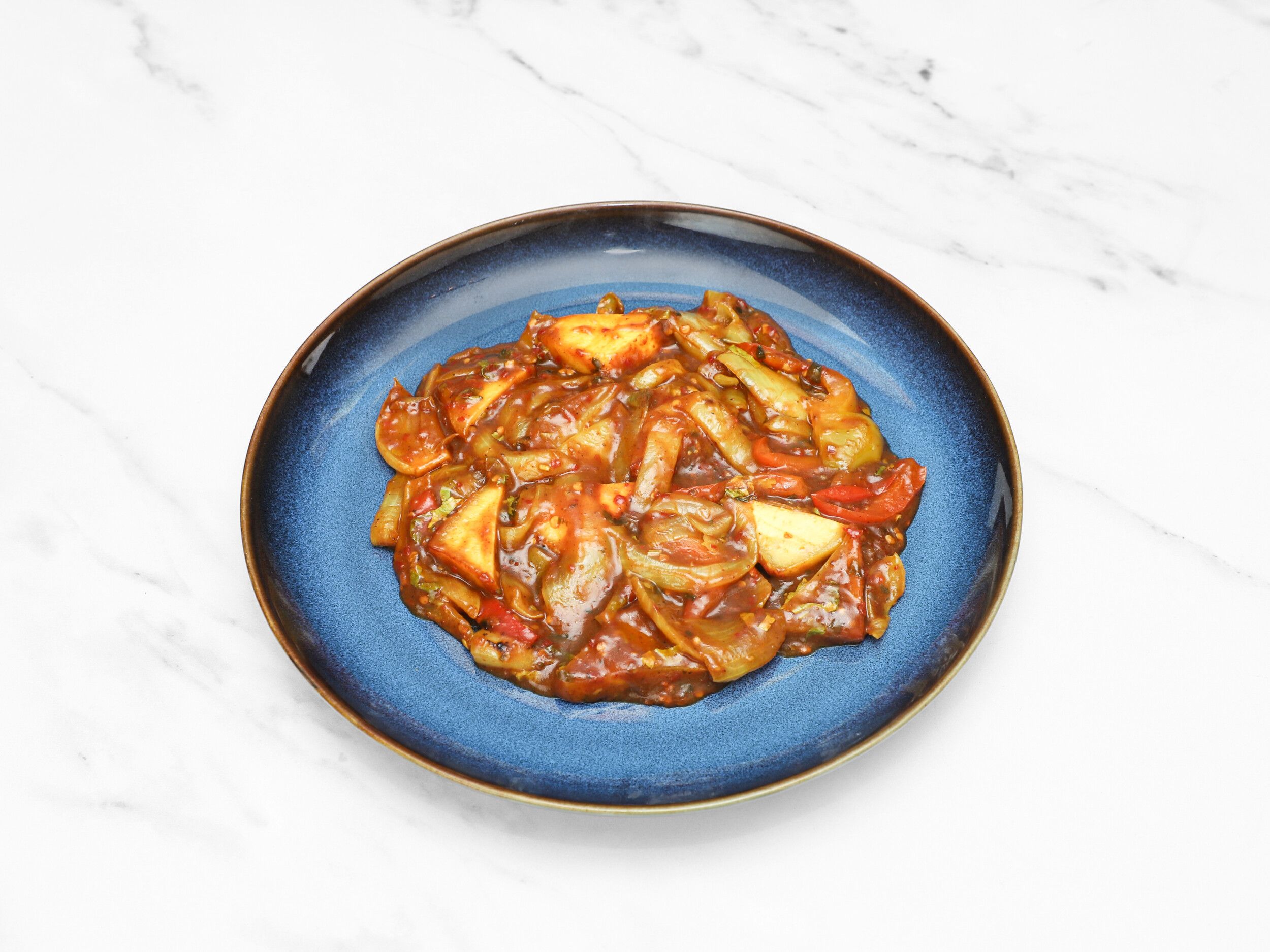 Chilli paneer with large onion and pepper pieces in a rich sauce on a blue plate