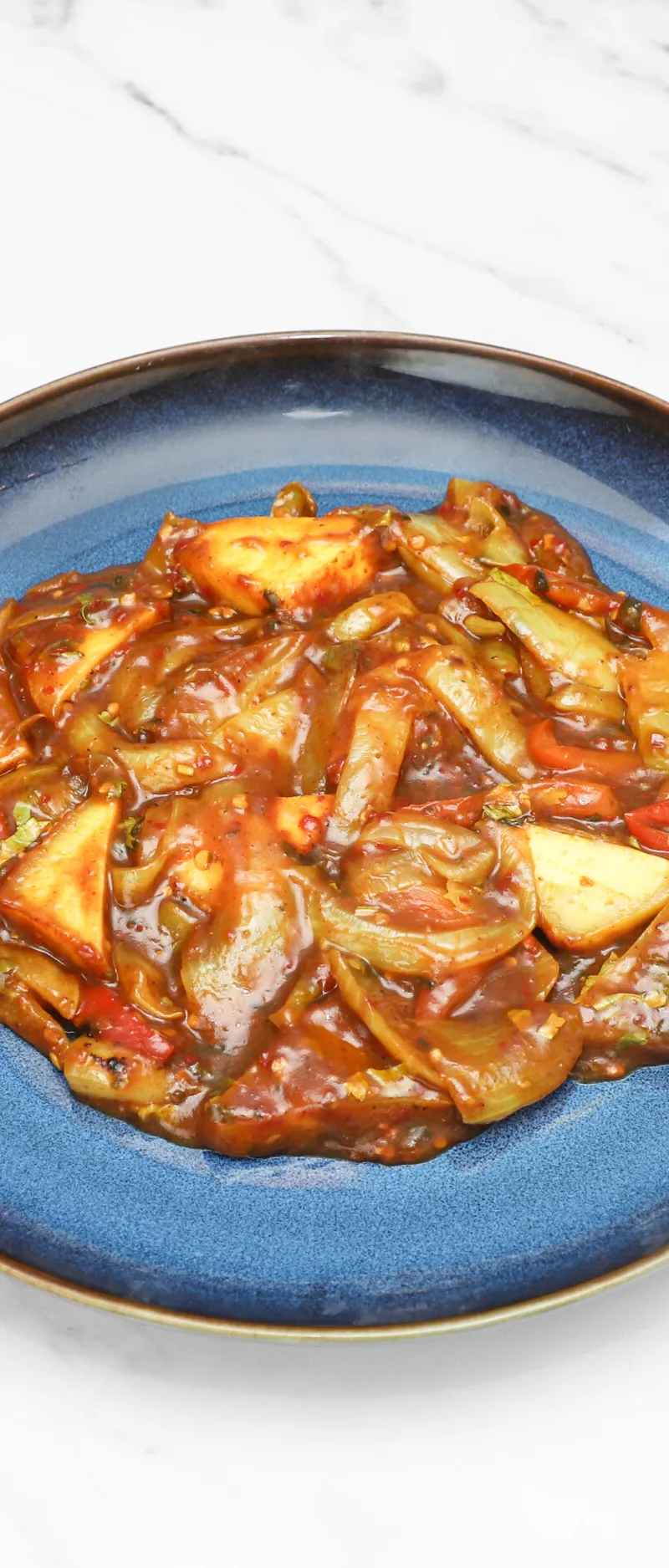 Chilli paneer with large onion and pepper pieces in a rich sauce on a blue plate