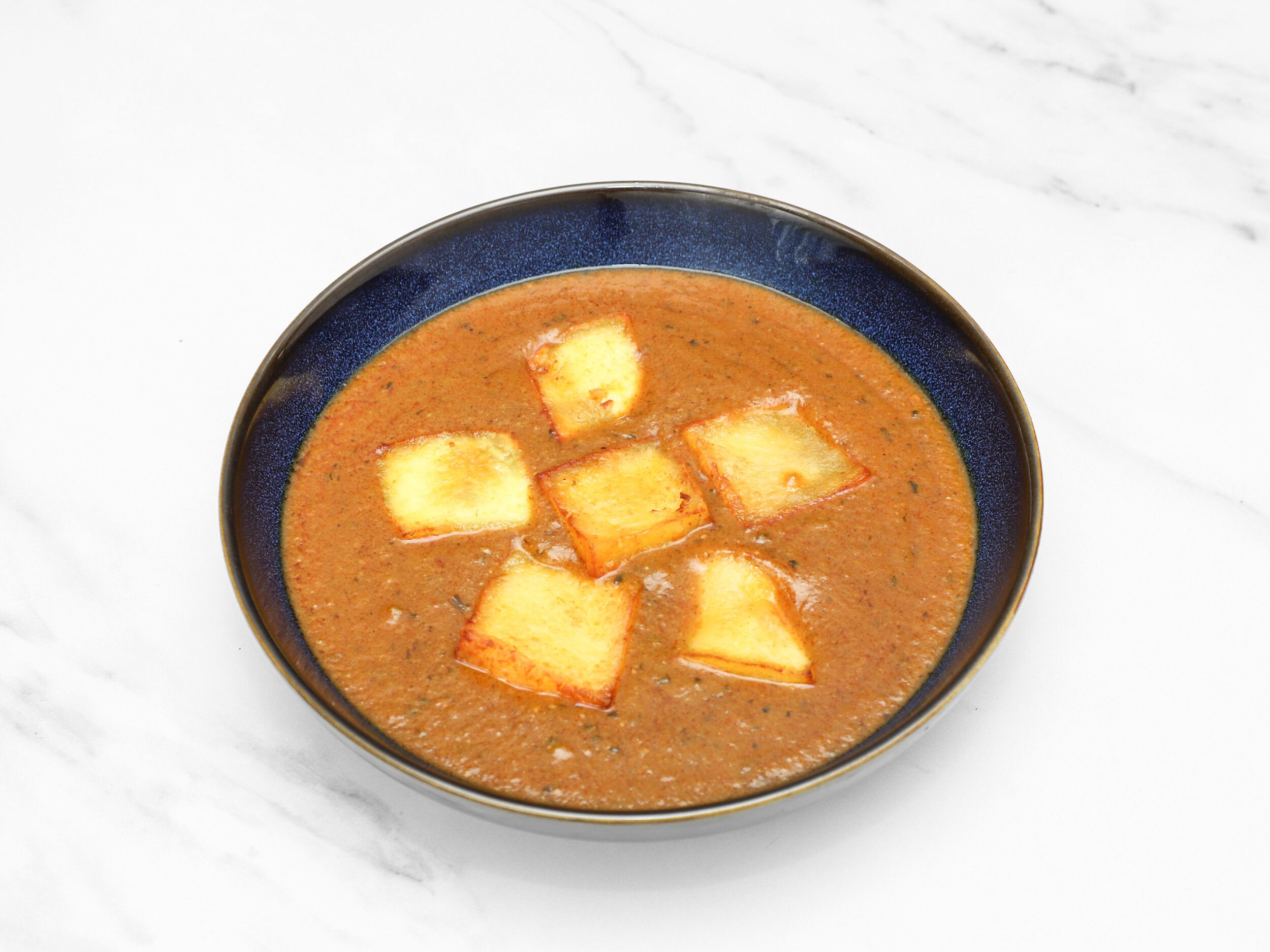 Top-down view of a dark blue bowl filled with a brown curry and five fried halloumi pieces.