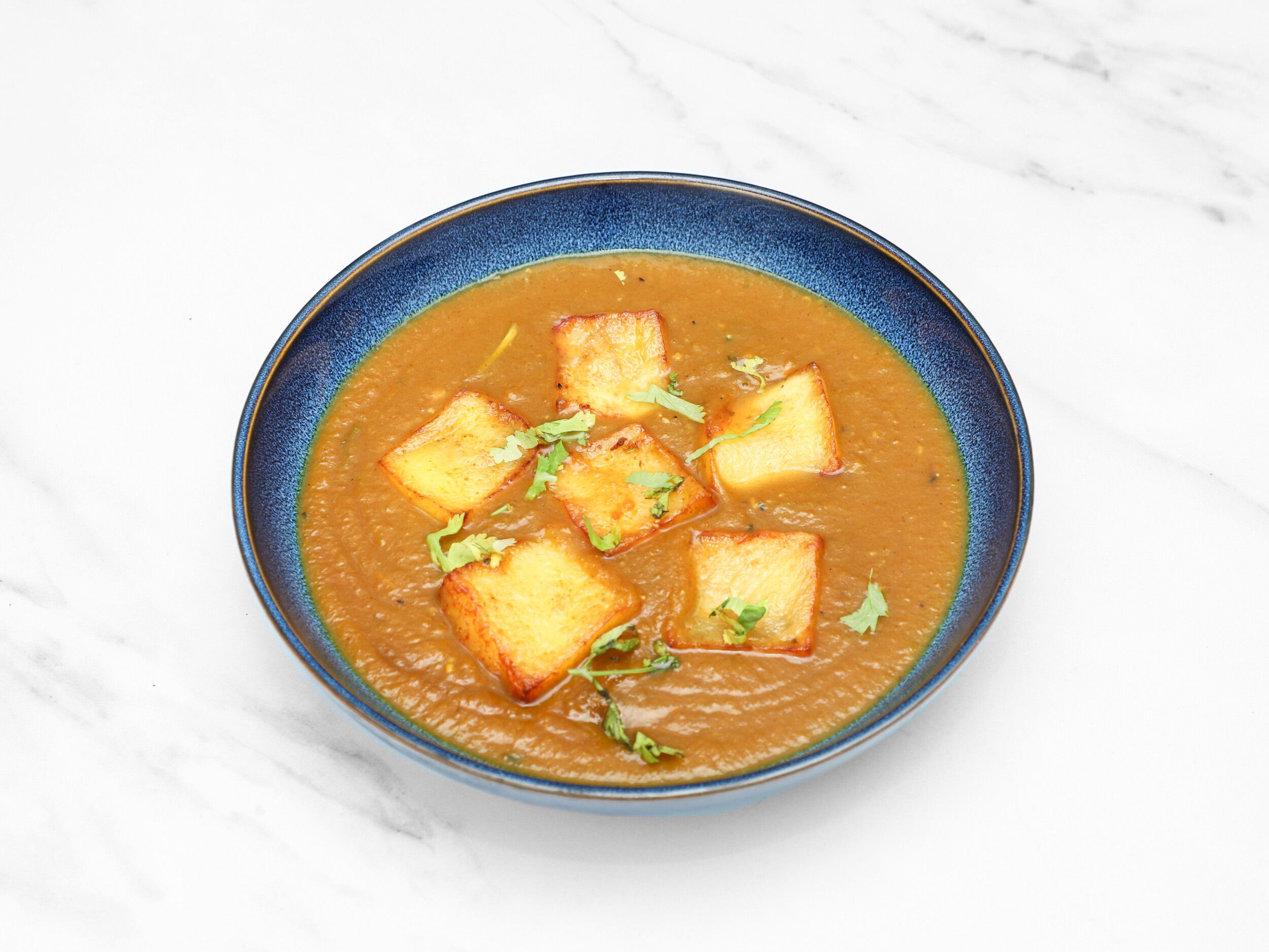 Golden fried paneer cheese squares in a rich, orange-brown curry, garnished with fresh cilantro leaves.
