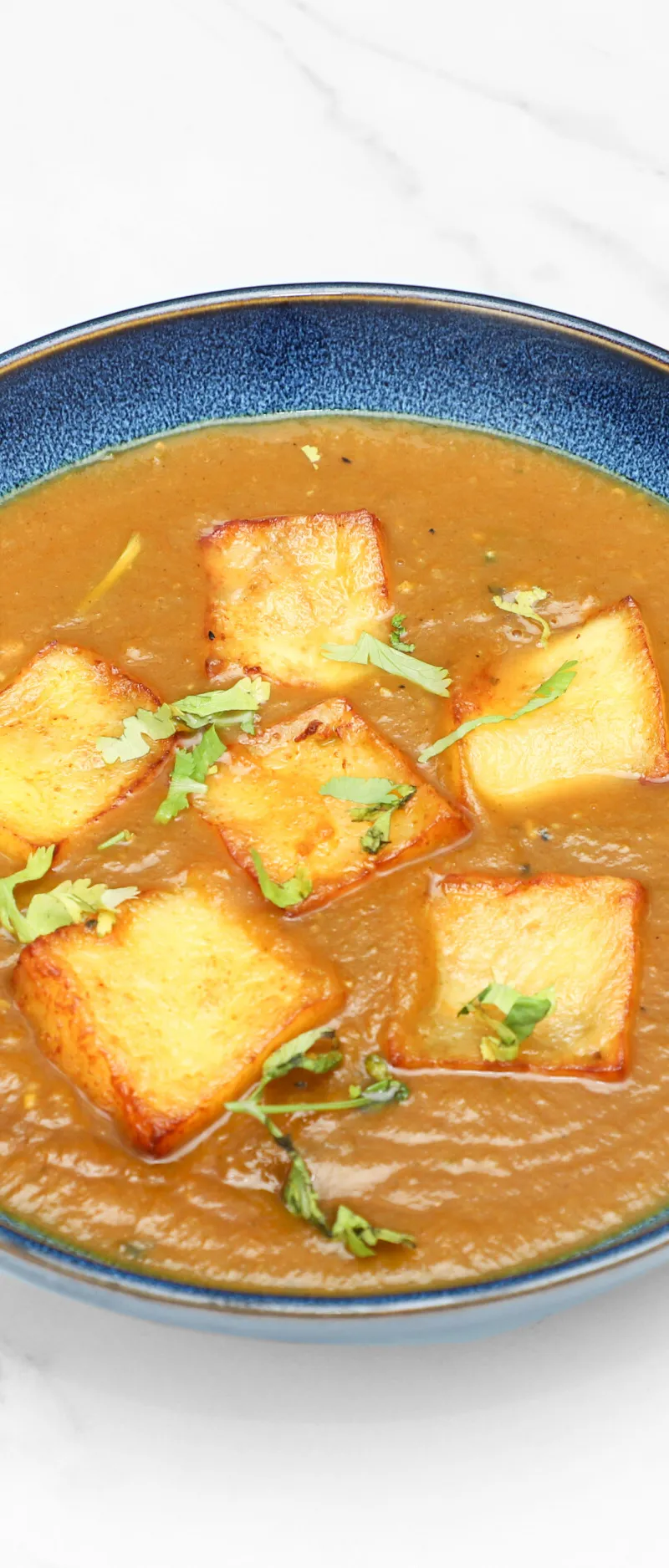 Golden fried paneer cheese squares in a rich, orange-brown curry, garnished with fresh cilantro leaves.