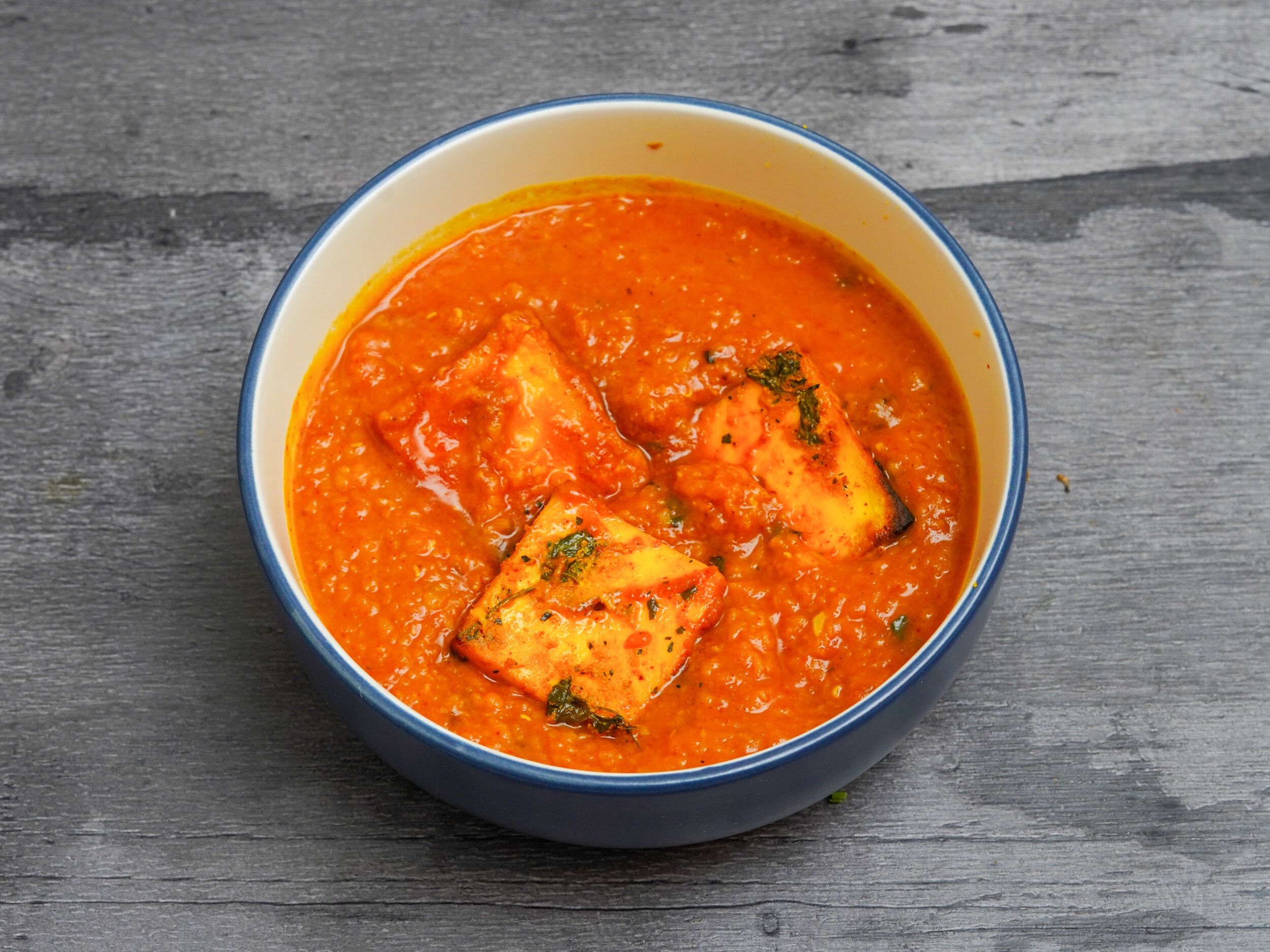 Indian paneer curry with orange sauce and three pieces of paneer in a blue ceramic bowl