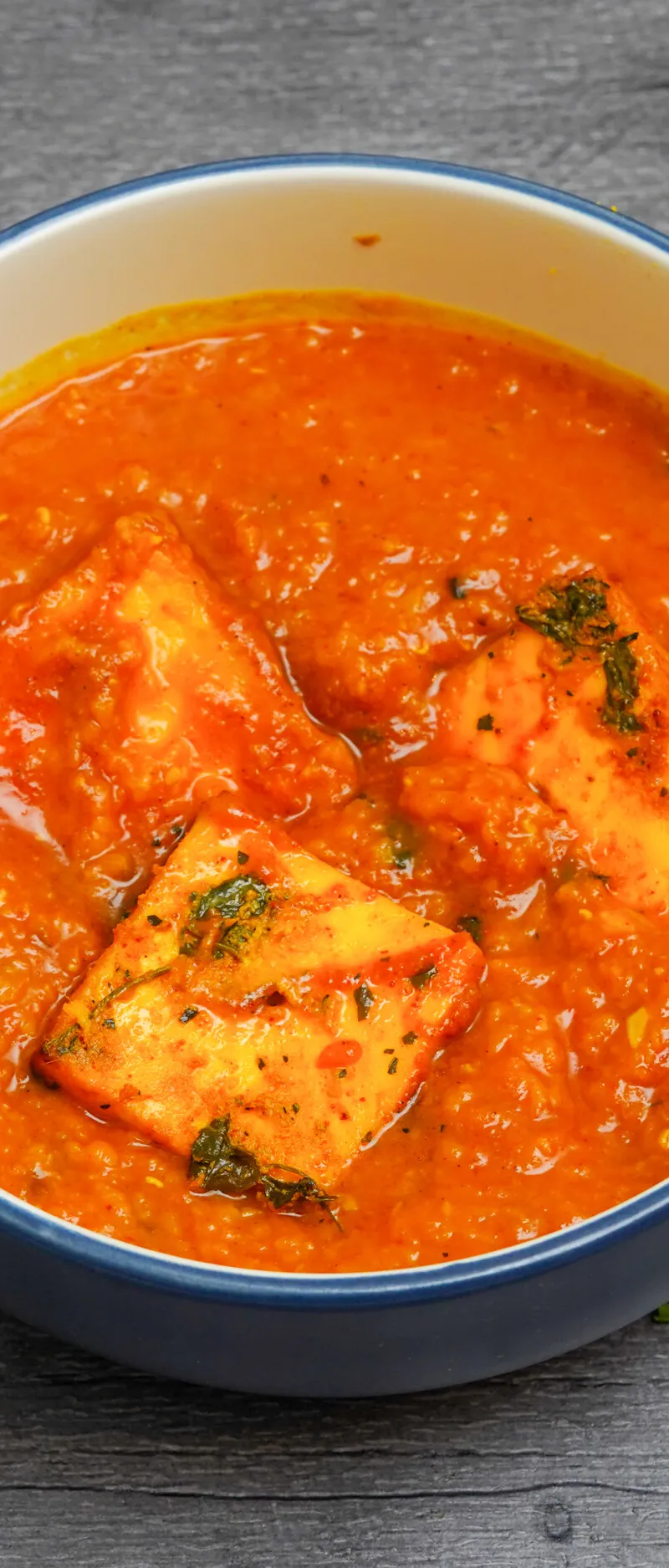 Indian paneer curry with orange sauce and three pieces of paneer in a blue ceramic bowl
