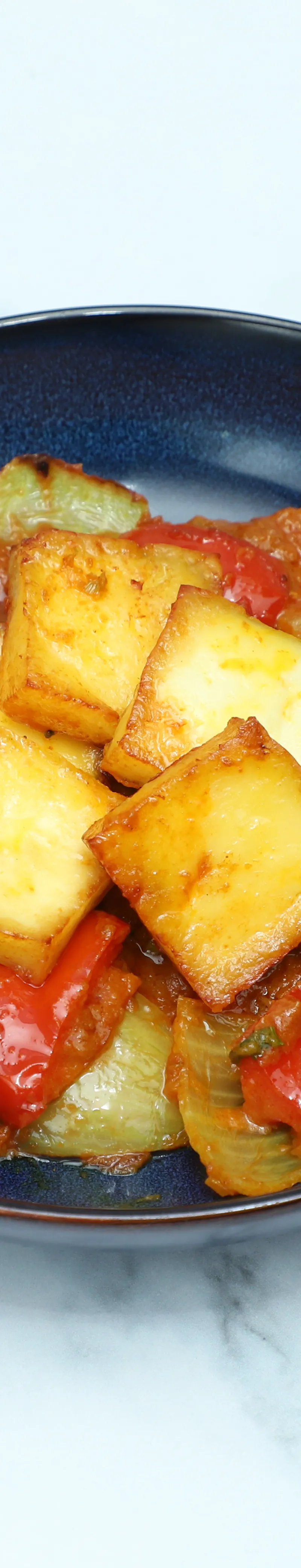 Golden paneer cubes with green and red bell peppers in a rich orange sauce, served in a deep blue bowl.