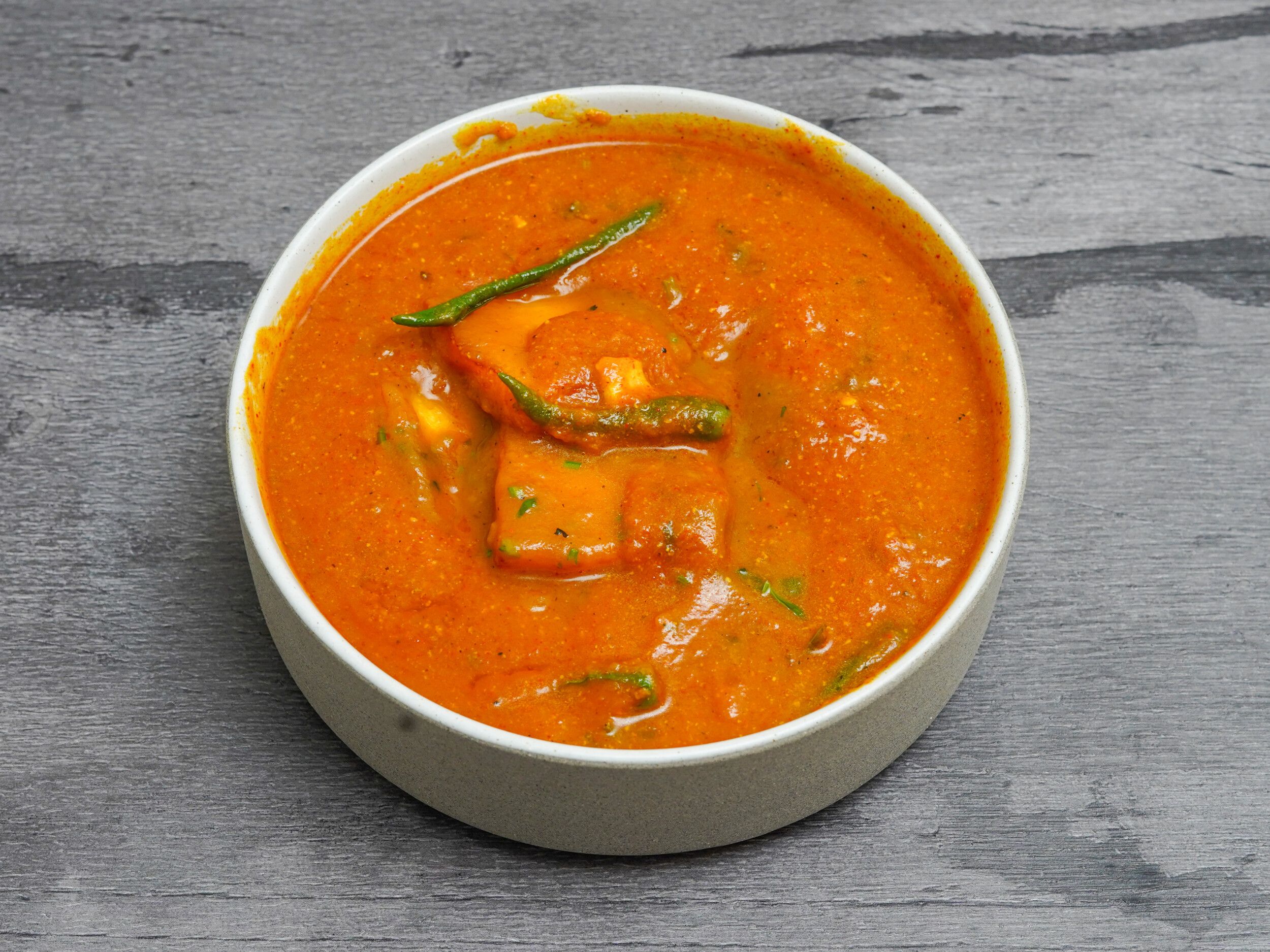 A white bowl containing rich orange paneer makhani garnished with green chilies and cilantro.