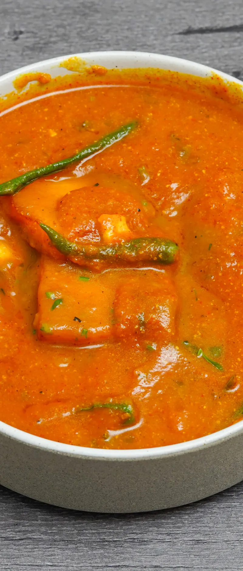 A white bowl containing rich orange paneer makhani garnished with green chilies and cilantro.