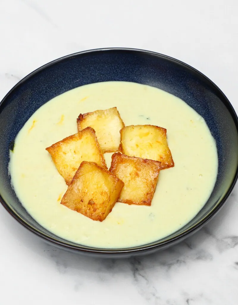 Pale yellow creamy soup with five golden-brown fried halloumi squares in a dark blue bowl.