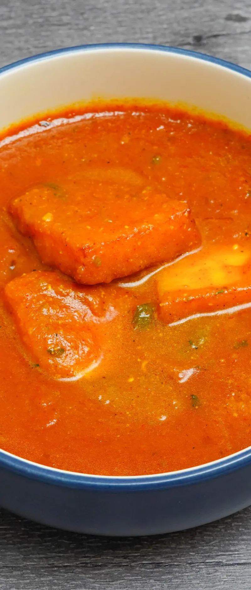 Bright orange paneer curry served in a blue bowl with a white rim on a wooden surface.