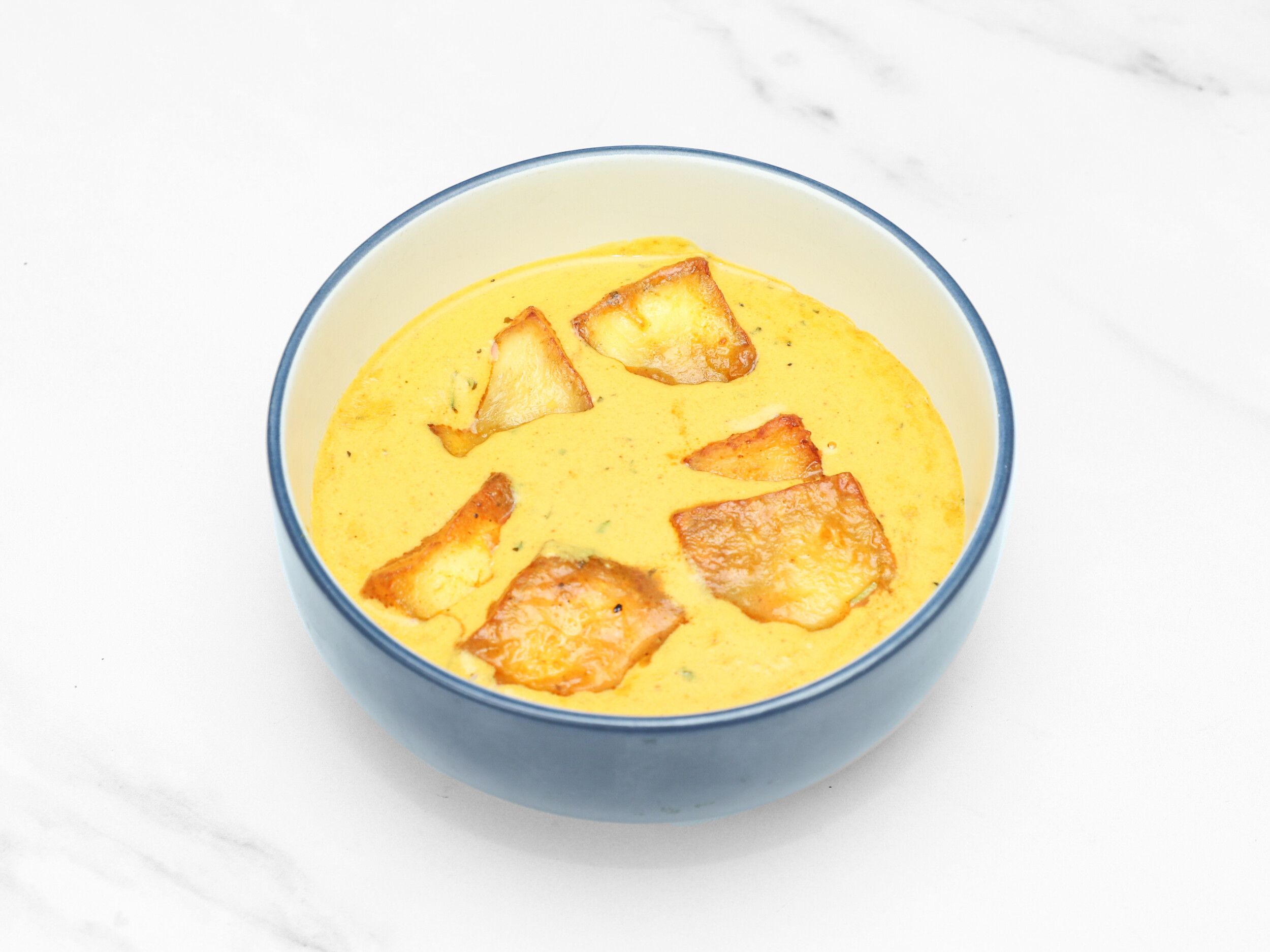 Golden yellow curry with several pieces of fried fritter floating in a blue bowl