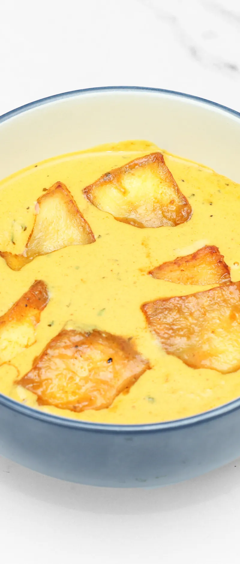 Golden yellow curry with several pieces of fried fritter floating in a blue bowl