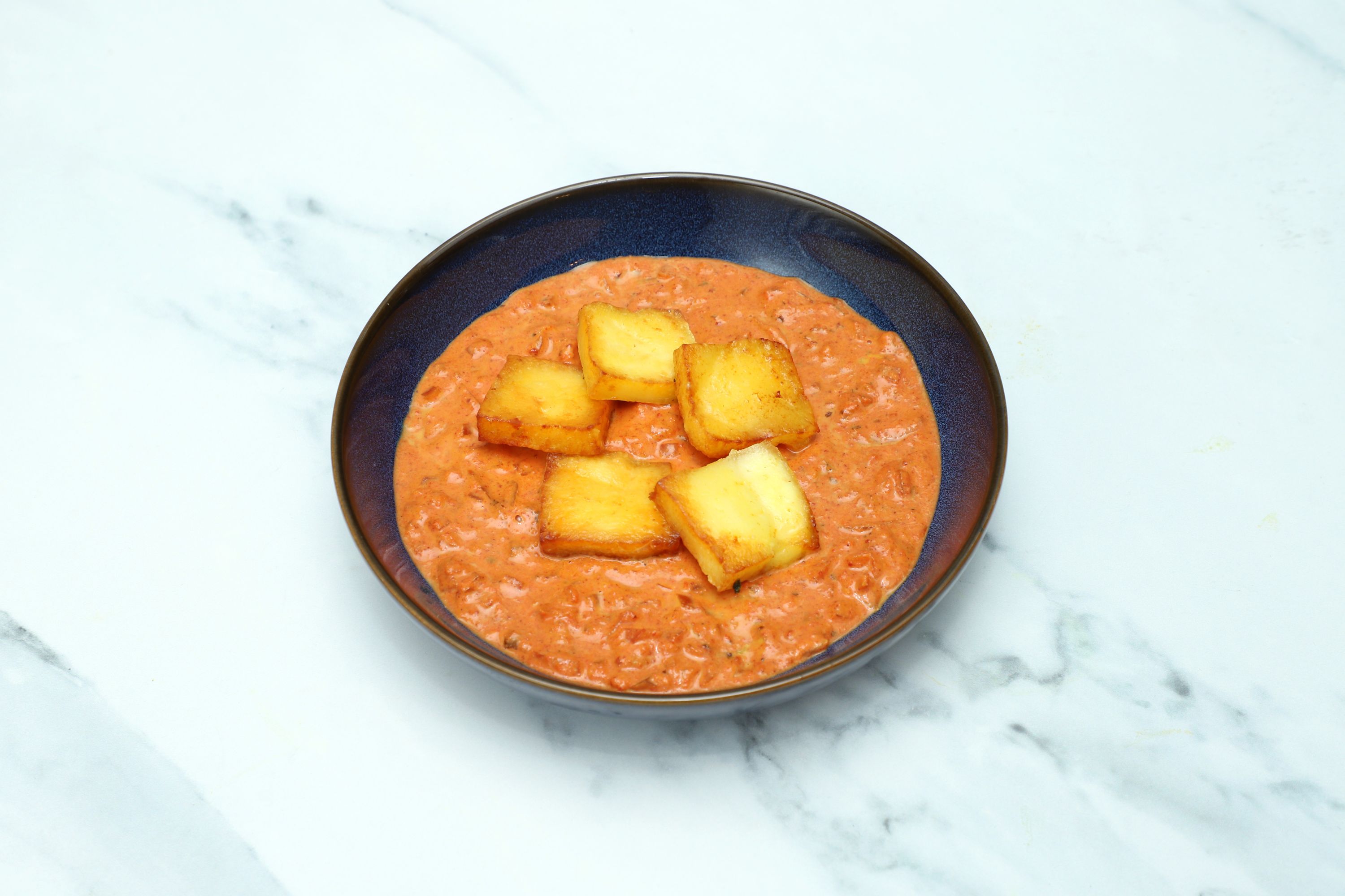 Golden brown paneer cubes floating in a rich orange-red creamy sauce in a modern blue bowl