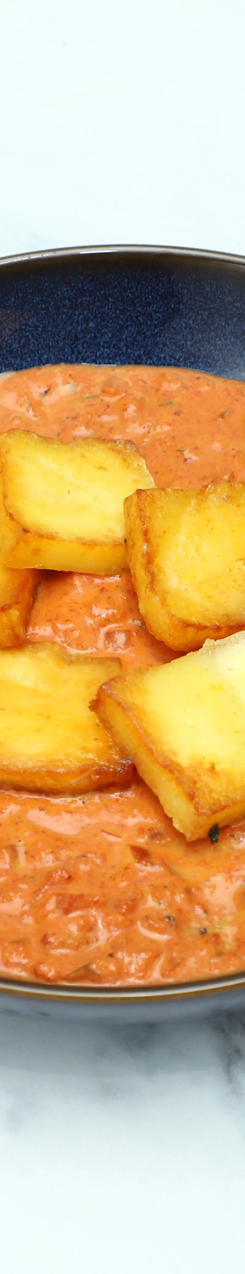 Golden brown paneer cubes floating in a rich orange-red creamy sauce in a modern blue bowl
