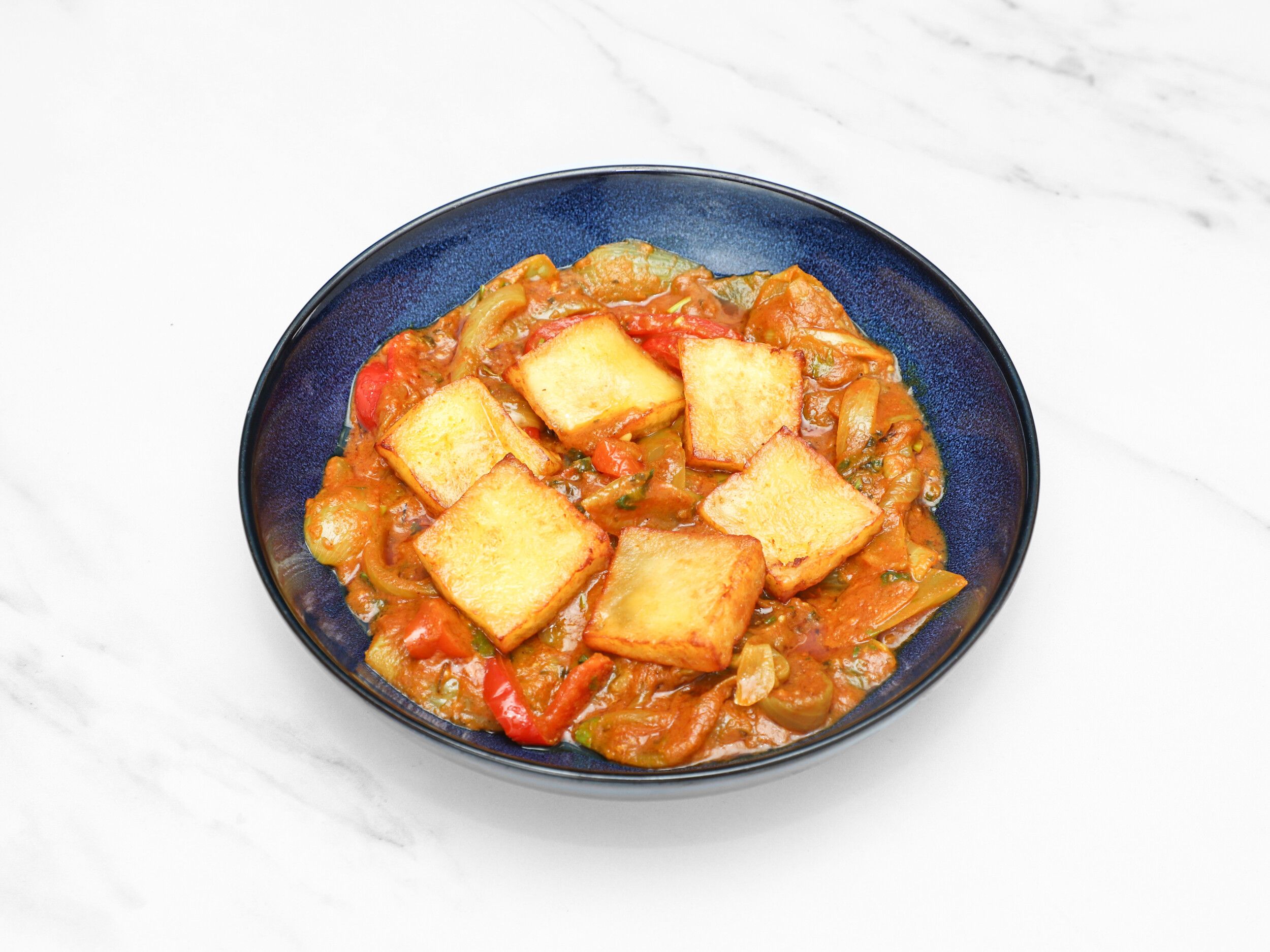Golden-fried paneer cubes in a rich, orange-red curry with green and red peppers and onions.