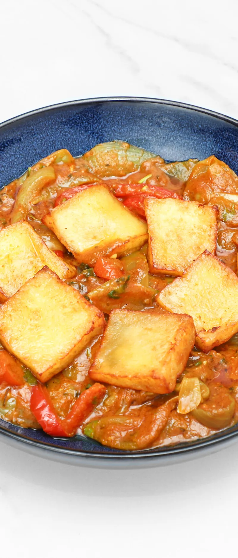 Golden-fried paneer cubes in a rich, orange-red curry with green and red peppers and onions.