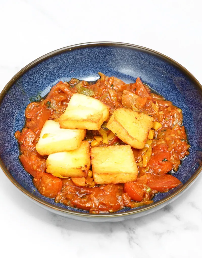 Golden-brown fried paneer cubes resting on a vibrant red tomato and vegetable curry in a dark blue bowl.